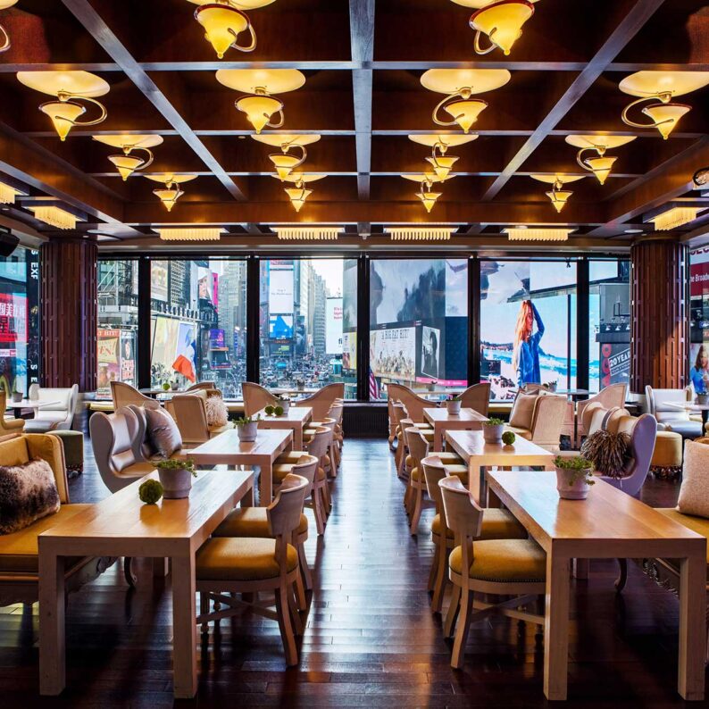 a room full of empty lounge tables surrounded by large windows overlooking Times Square in the day